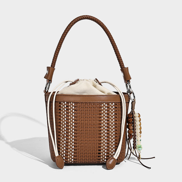 Small woven bucket bag with drawstring top, braided handle, detachable crossbody strap, and silver-tone ring hardware, detail