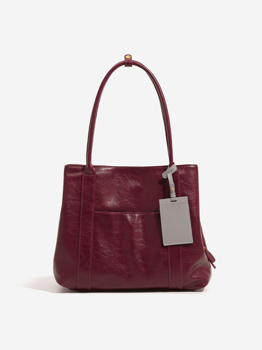 Structured trapezoid tote bag in dark chocolate leather-look finish with long shoulder straps, front slip pocket, and, detail