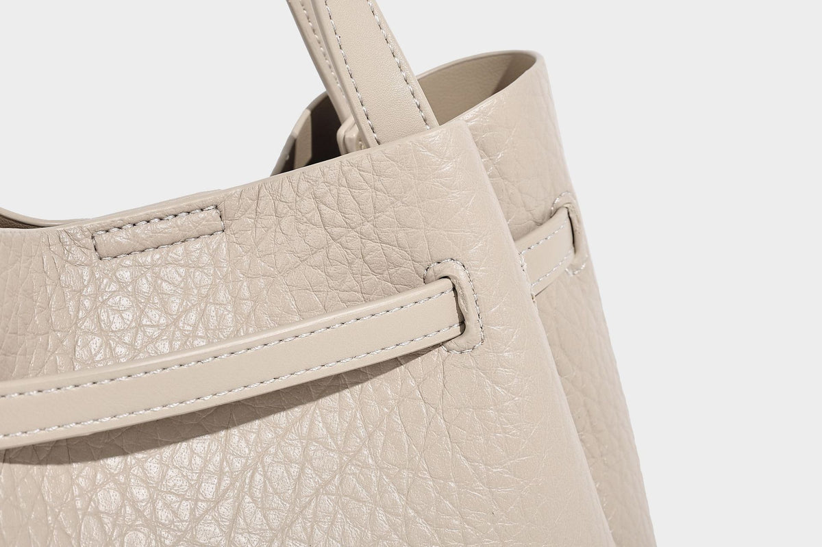 Small structured pebbled bucket tote with double top handles, silver turn-lock hardware, and detachable shoulder strap