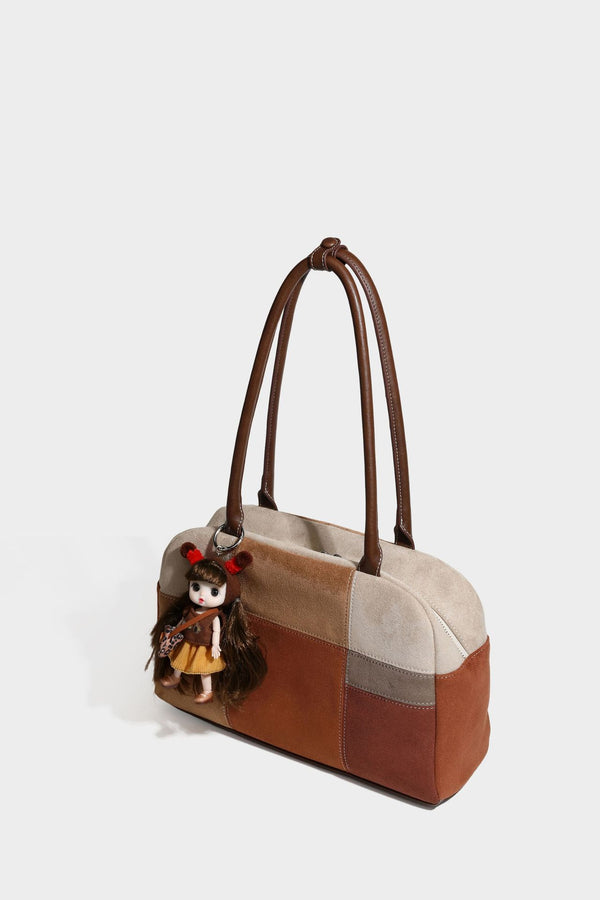 Boxy patchwork suede-look shoulder tote in tan, beige, rust, and brown panels with double brown straps and hanging doll