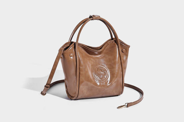 Glossy leather-look structured tote bag with rounded top handles, detachable shoulder strap, embossed front emblem, and side