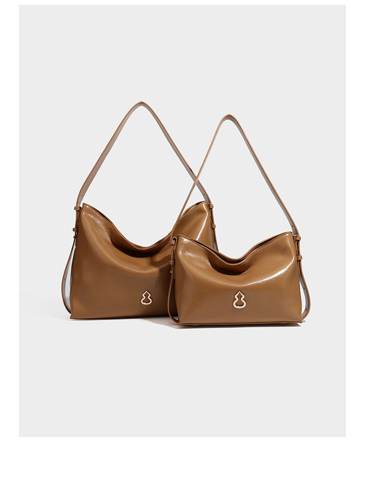 Lässige Hobo-Schultertasche mit offenem oberen Abschluss in glänzender karamellfarbener Lederoptik mit goldfarbenen Logo-Beschlägen und langem, verstellbarem