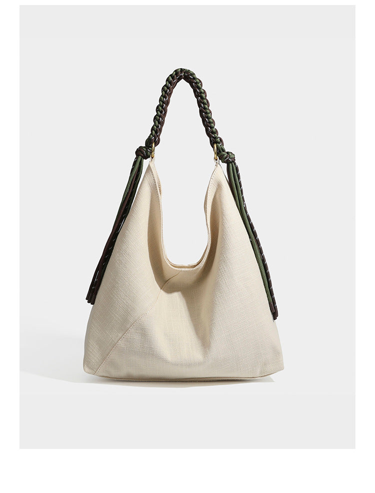 Soft slouchy cream canvas shoulder tote with braided brown and green cord handle, gold-tone ring hardware, and tassel trim