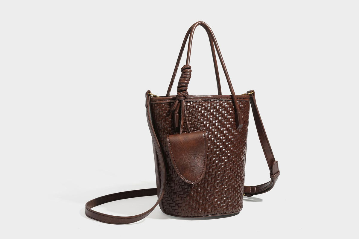 Structured woven-texture leather-look bucket bag in brown with knotted top handles, small front flap pouch, and adjustable