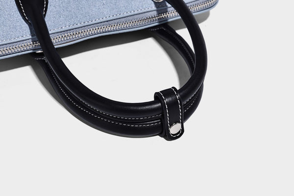 Compact structured satchel in light blue denim-look fabric with black leather-look trim, silver turn-lock closure, rolled