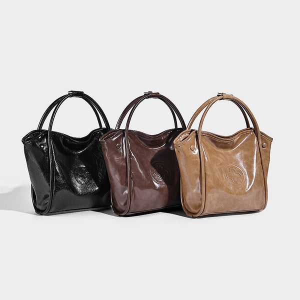 Glossy leather-look structured tote bag with rounded top handles, detachable shoulder strap, embossed front emblem, and side