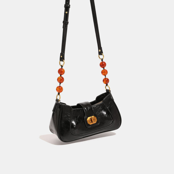 Compact glossy crinkled baguette shoulder bag with amber resin bead strap accent and gold-tone turn-lock closure, front view