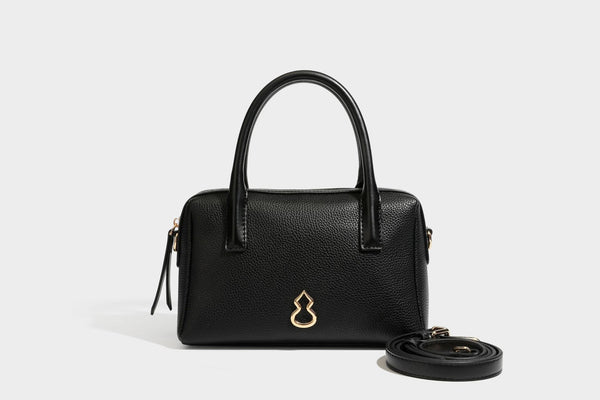 Small structured pillow satchel bag with pebbled leather-look finish, dual rolled top handles, gold-tone gourd emblem, and