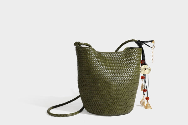 Olive green woven leather-look bucket bag with braided crossbody strap, knotted adjustment, and gold-tone tassel charm with