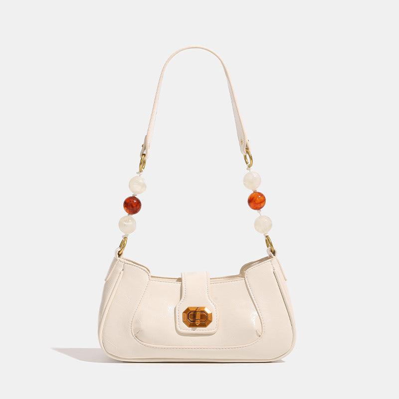 Compact glossy crinkled baguette shoulder bag with amber resin bead strap accent and gold-tone turn-lock closure, detail view