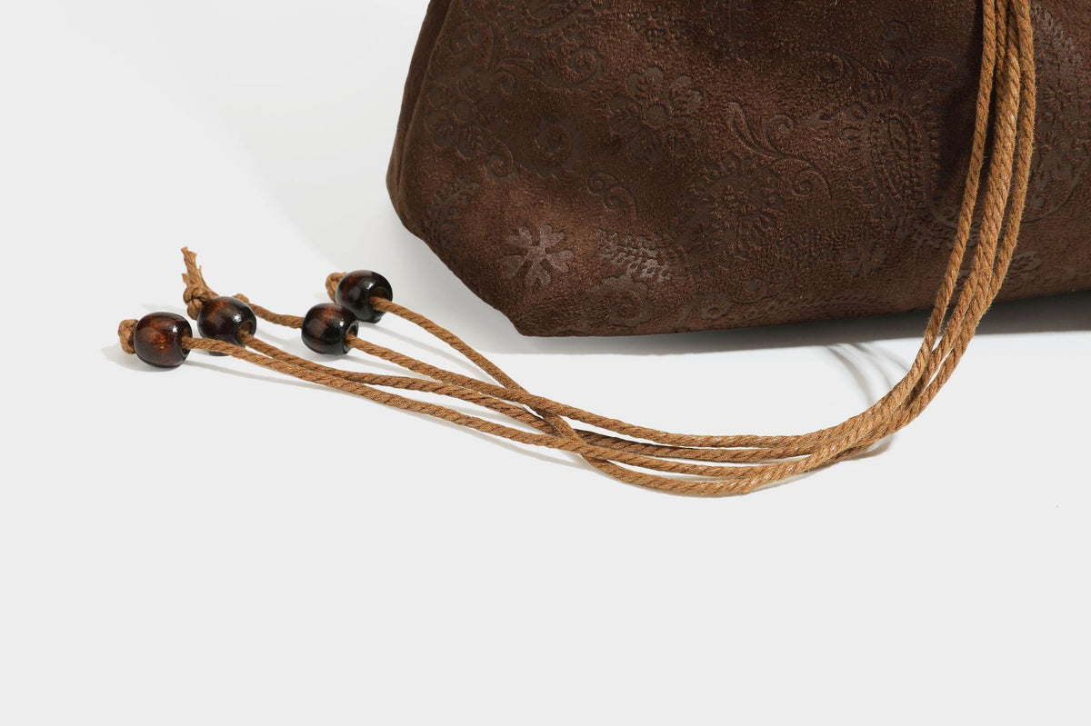 Slouchy boho hobo shoulder bag in embossed brown suede-look finish with beaded strap, cord tassels, and brass-tone leaf