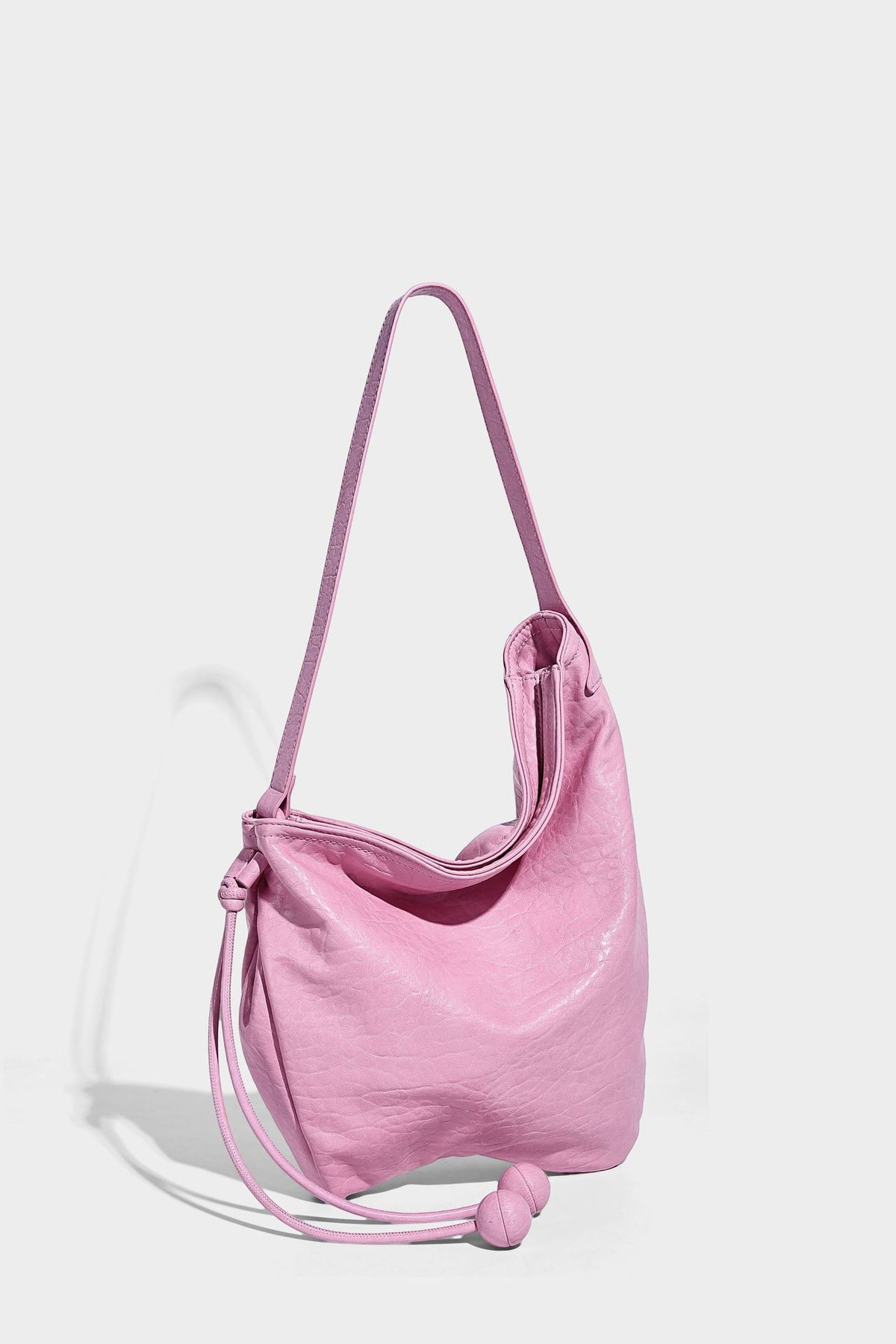 Slouchy hobo shoulder bag in pale yellow with slim strap, drawstring bead closure, and pink tulip floral charm, detail view