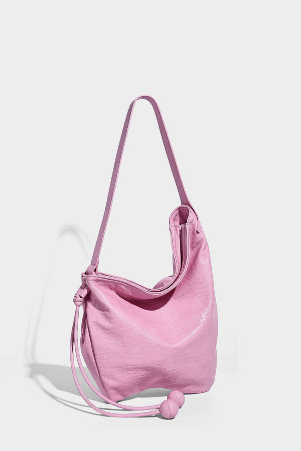 Slouchy hobo shoulder bag in pale yellow with slim strap, drawstring bead closure, and pink tulip floral charm, detail view