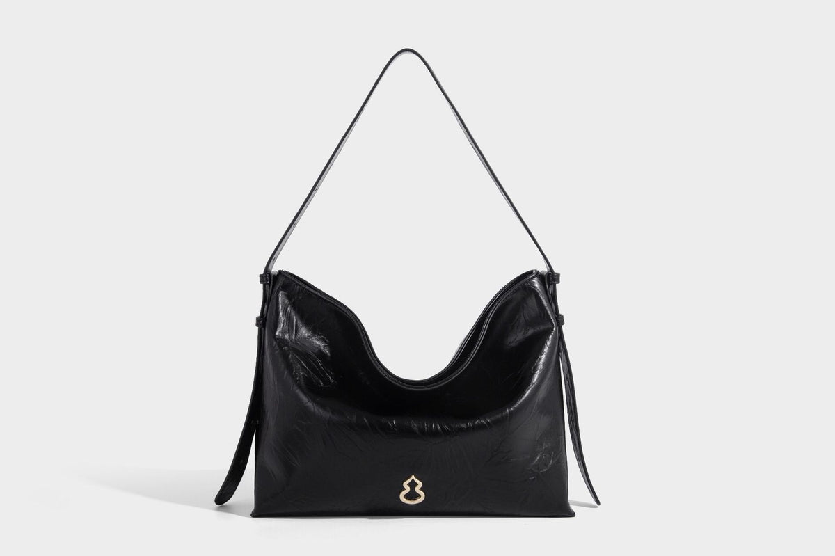 Large slouchy hobo shoulder bag in glossy crinkle leather-look finish with gold-tone emblem hardware and adjustable strap