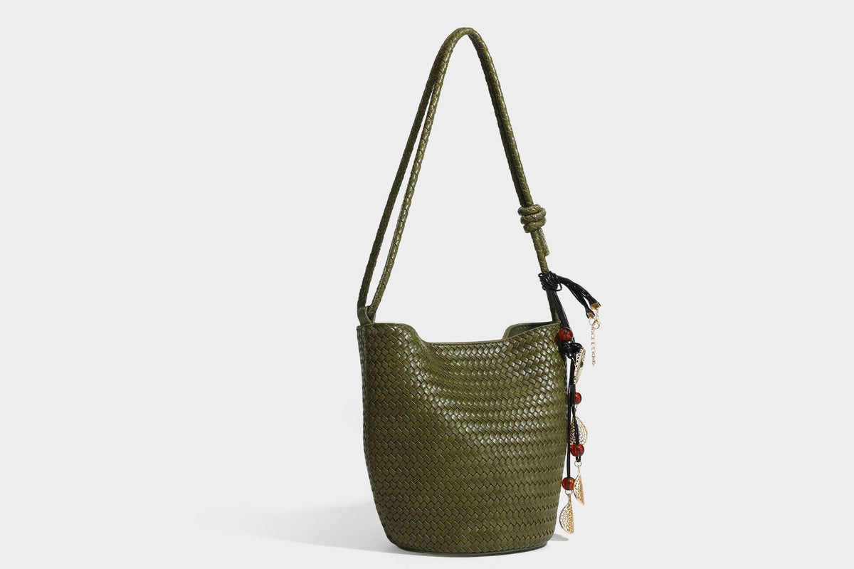 Olive green woven leather-look bucket bag with braided crossbody strap, knotted adjustment, and gold-tone tassel charm with
