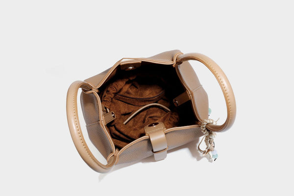 Pebbled leather-look bucket tote bag with rolled double handles, drawstring closure, braided cord charm, and detachable