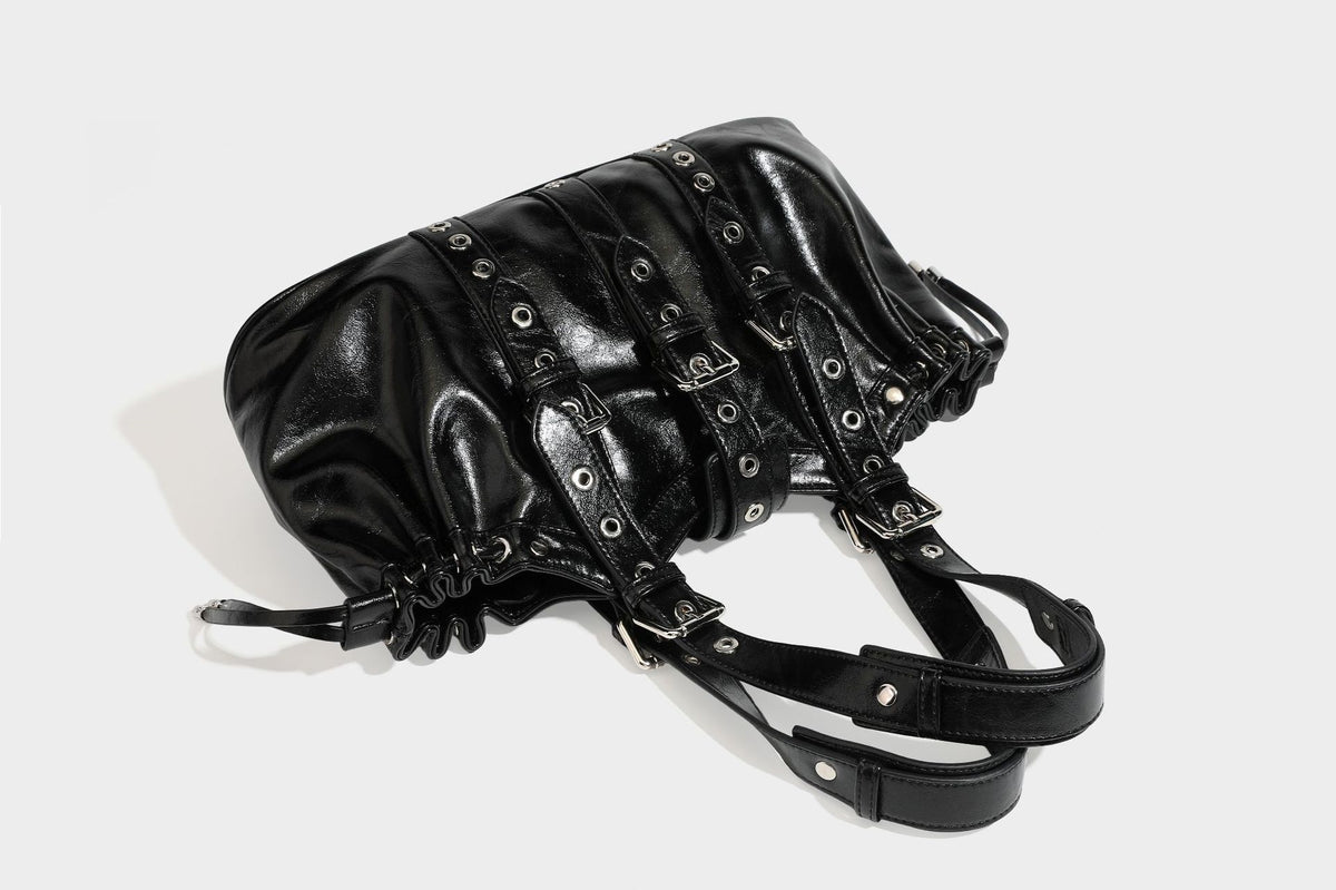 Large black glossy leather-look tote bag with silver buckle straps, eyelet grommet panels, drawstring side gathers, and