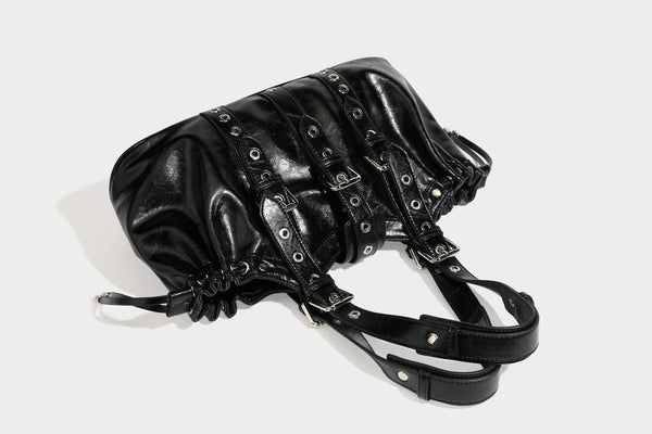Large black glossy leather-look tote bag with silver buckle straps, eyelet grommet panels, drawstring side gathers, and