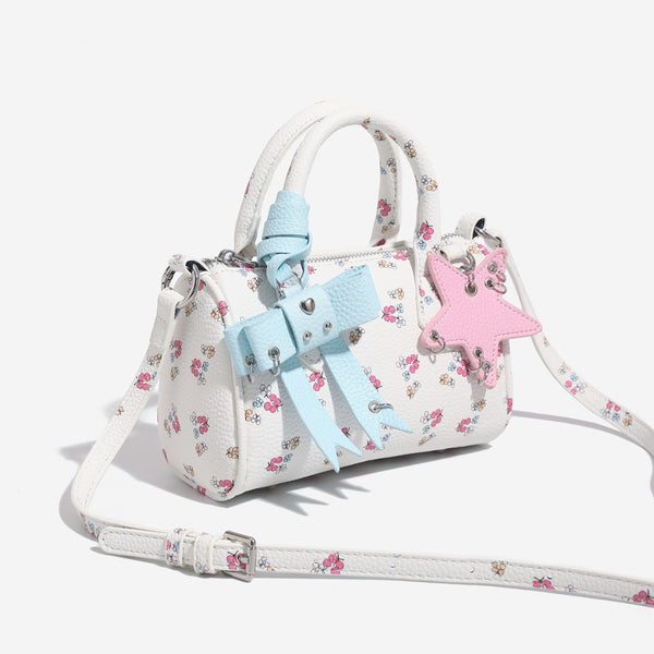 Weiße Mini-Boston-Handtasche mit genarbter Oberfläche und Blumen- oder Kirschprint, pastellblauem Schleifenanhänger, rosafarbenem Sternanhänger und zwei oberen Henkeln