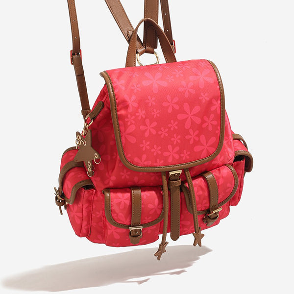 Red floral-print backpack handbag with brown leather-look trim, dual front buckle pockets, star charms, and gold-tone, detail