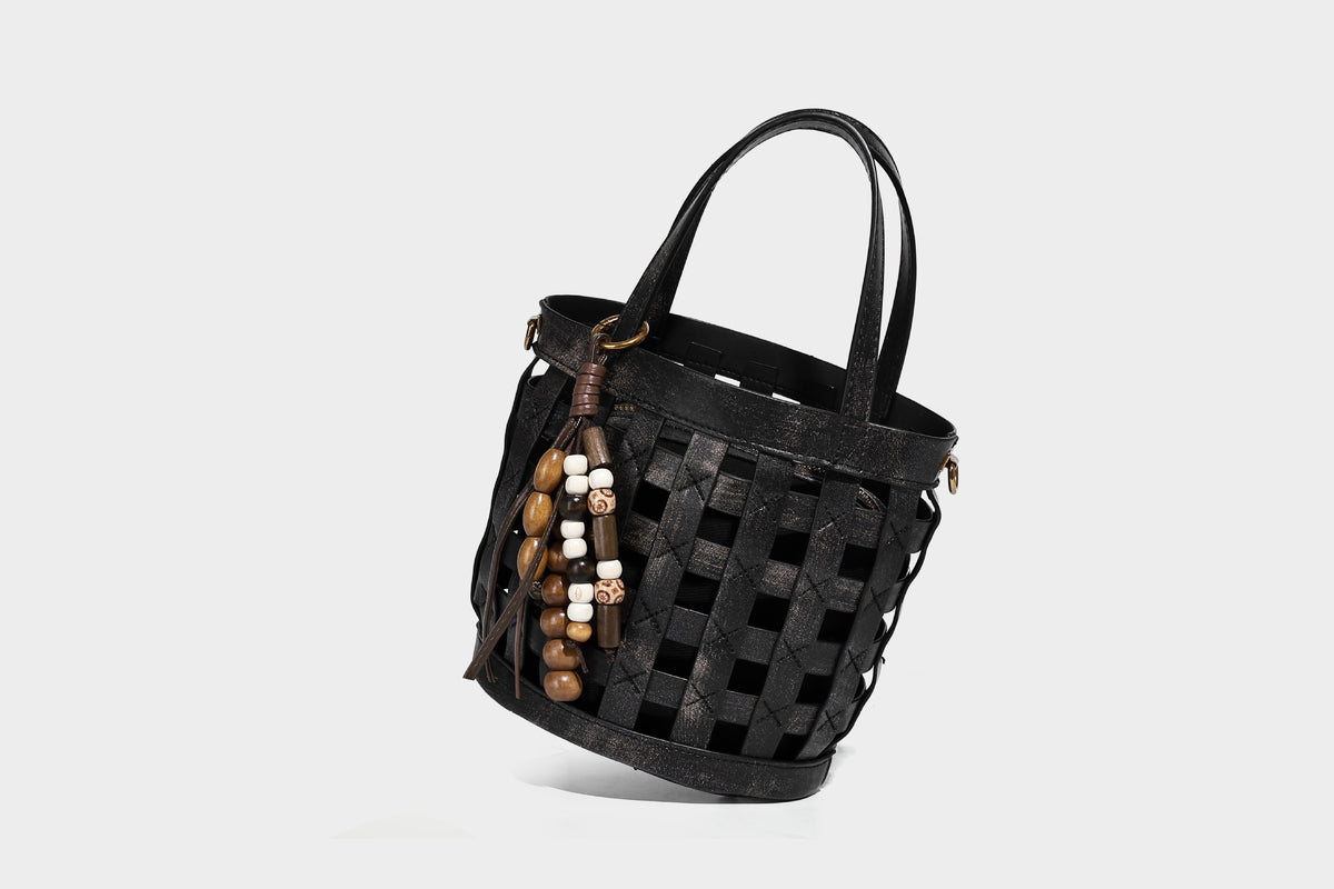 Small woven lattice bucket bag in brown leather-look finish with beaded tassel charm, dual top handles, and detachable