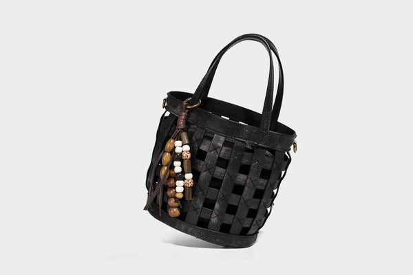 Small woven lattice bucket bag in brown leather-look finish with beaded tassel charm, dual top handles, and detachable