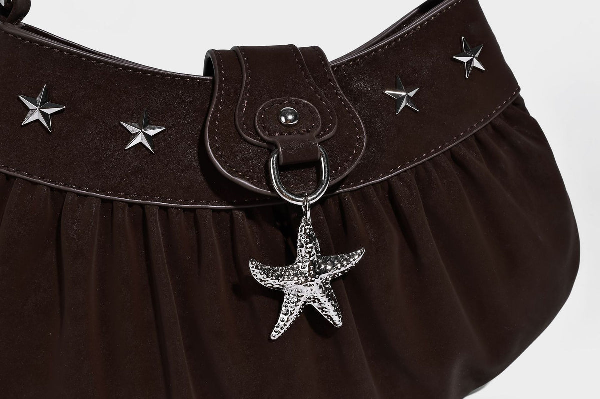 Ruched shoulder bag with curved flap, silver star studs, dangling starfish charm, and adjustable crossbody strap, detail view