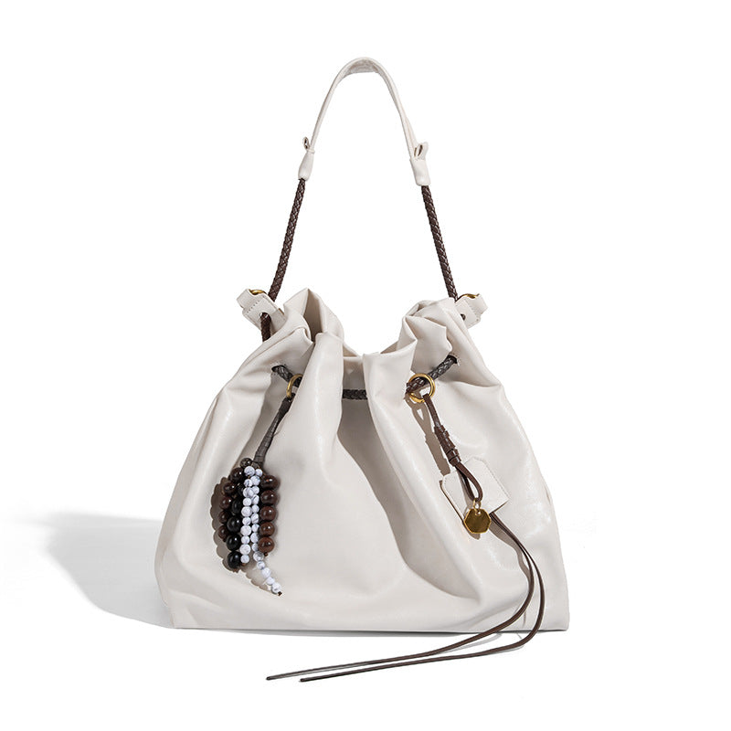 Cream slouchy drawstring bucket bag with braided cord, beaded tassel charm, and gold-tone ring hardware, detail view 5