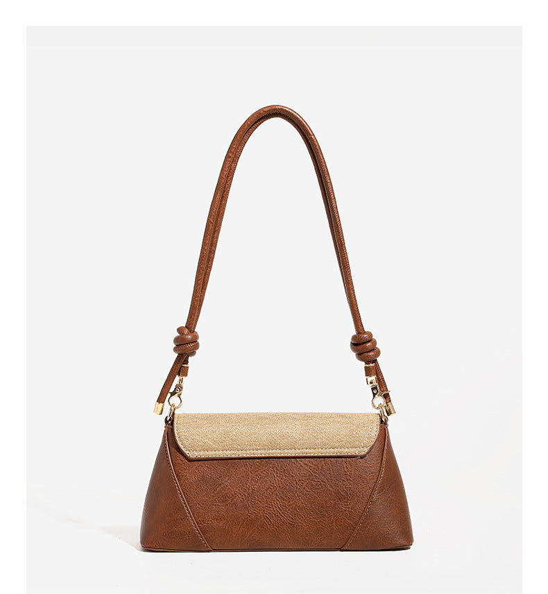 Structured trapezoid shoulder bag with pale textured flap, gold-tone triangular turn-lock closure, and long knotted cord