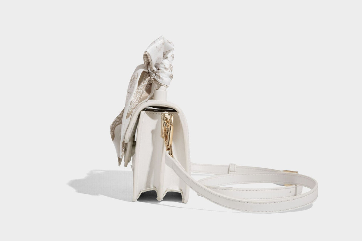Small structured white flap bag with butterfly embroidery, flower-shaped turn-lock clasp, braided top handle with scarf bow
