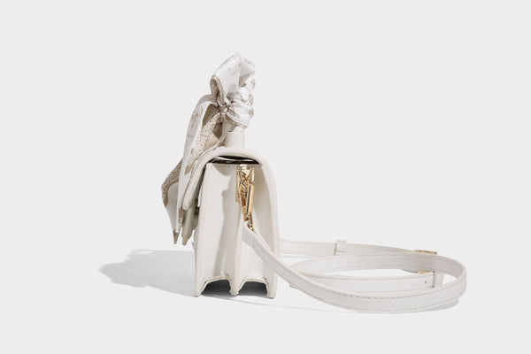 Small structured white flap bag with butterfly embroidery, flower-shaped turn-lock clasp, braided top handle with scarf bow