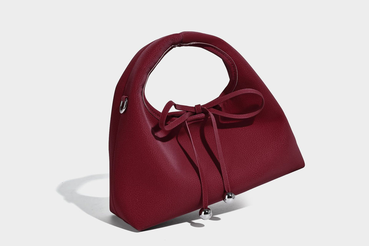 Pebbled matte trapezoid top-handle bag with drawstring bow closure, bead-tipped cords, silver-tone hardware, and detachable