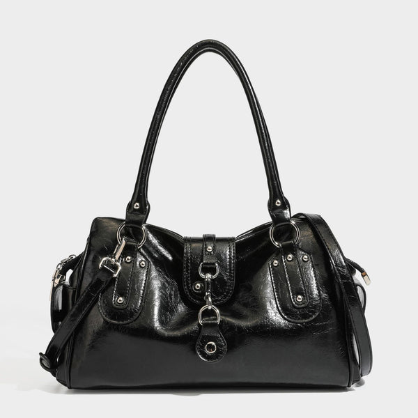 Glänzende, geknautschte Barrel-Satchel mit zwei oberen Tragegriffen, vorderem Klappen-Riemen-Panel, Ring- und Nietenbeschlägen sowie einem abnehmbaren