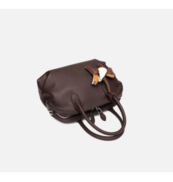 Rounded dome shell handbag in pebbled leather-look finish with twin top handles, zip closure, decorative horse charm, and