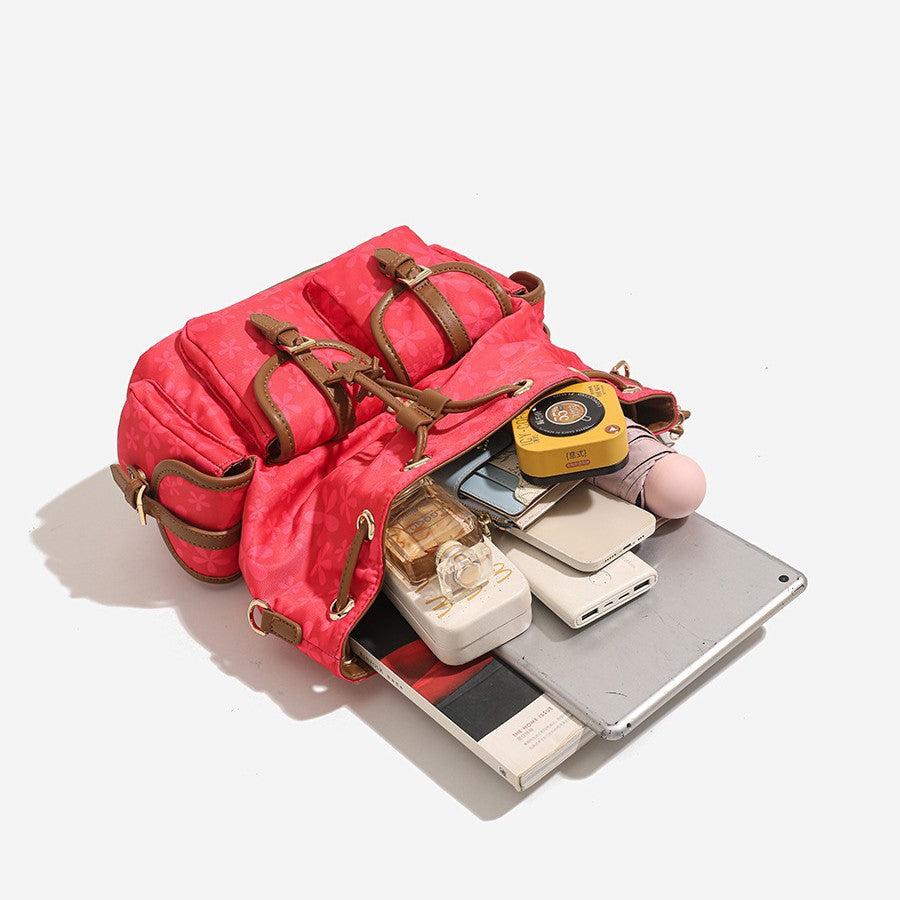 Red floral-print backpack handbag with brown leather-look trim, dual front buckle pockets, star charms, and gold-tone, detail