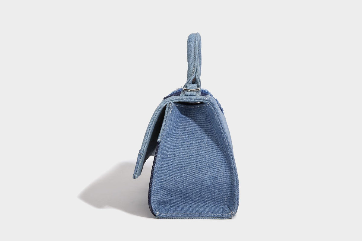 Structured patchwork denim trapezoid satchel bag with frayed panel trim, rounded top handle, and silver-tone hardware, detail