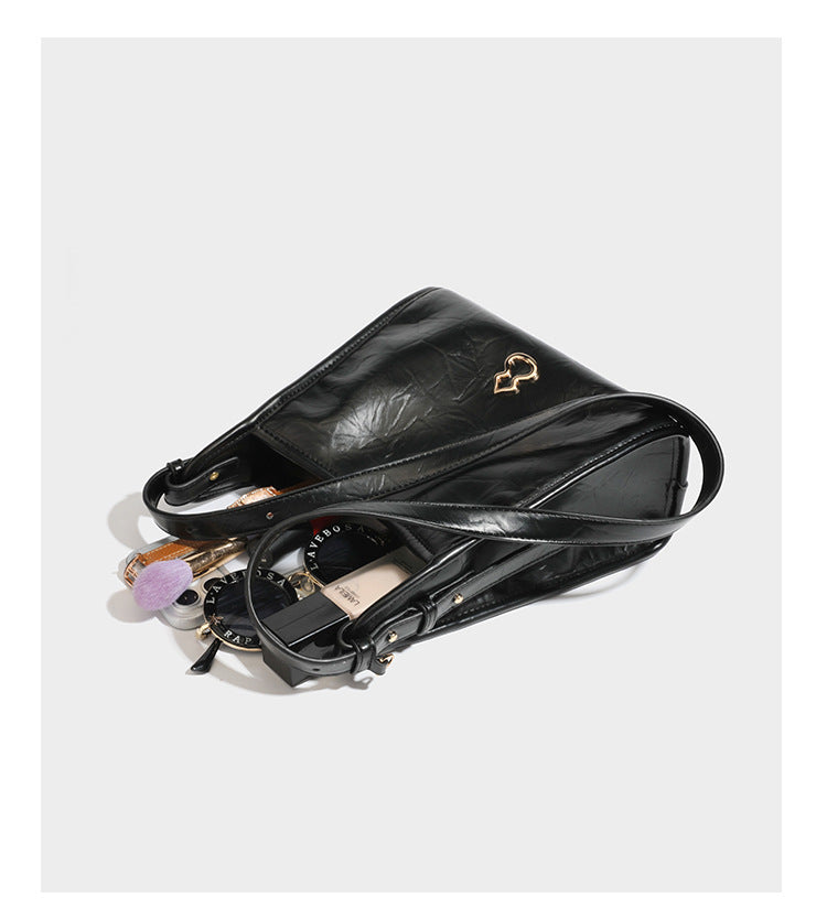 Strukturierte, trapezförmige Schultertasche aus glänzender, geknautscht wirkender Lederoptik mit goldfarbenen Beschlägen auf der Vorderseite und langem, verstellbarem
