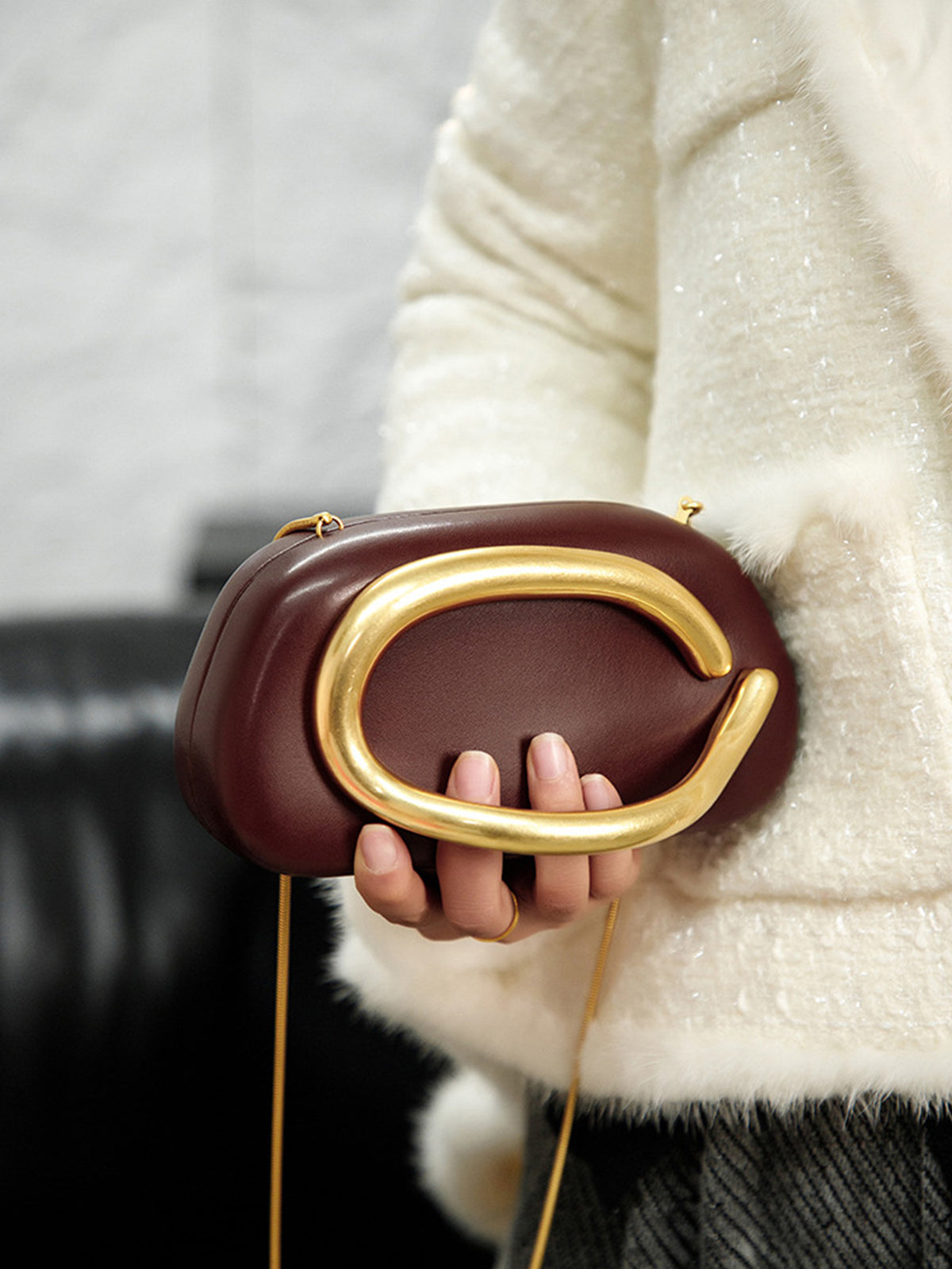 Kleine Crossbody-Clutch in abgerundeter Rechteckform mit übergroßem poliertem C-förmigem Goldhenkel und schmalem Goldkettenriemen, Detailansicht
