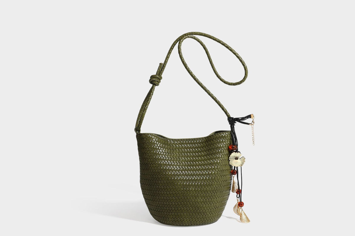 Olive green woven leather-look bucket bag with braided crossbody strap, knotted adjustment, and gold-tone tassel charm with