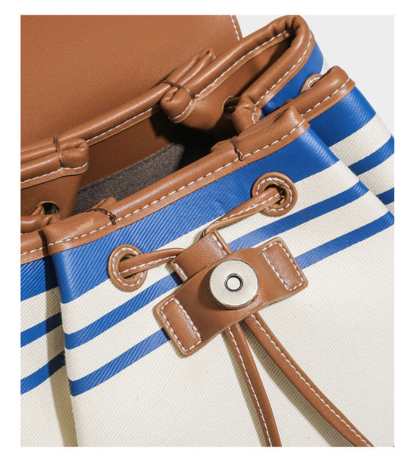 Cream canvas bucket bag with blue horizontal stripes, tan leather-look flap and trim, drawstring closure, silver-tone, detail