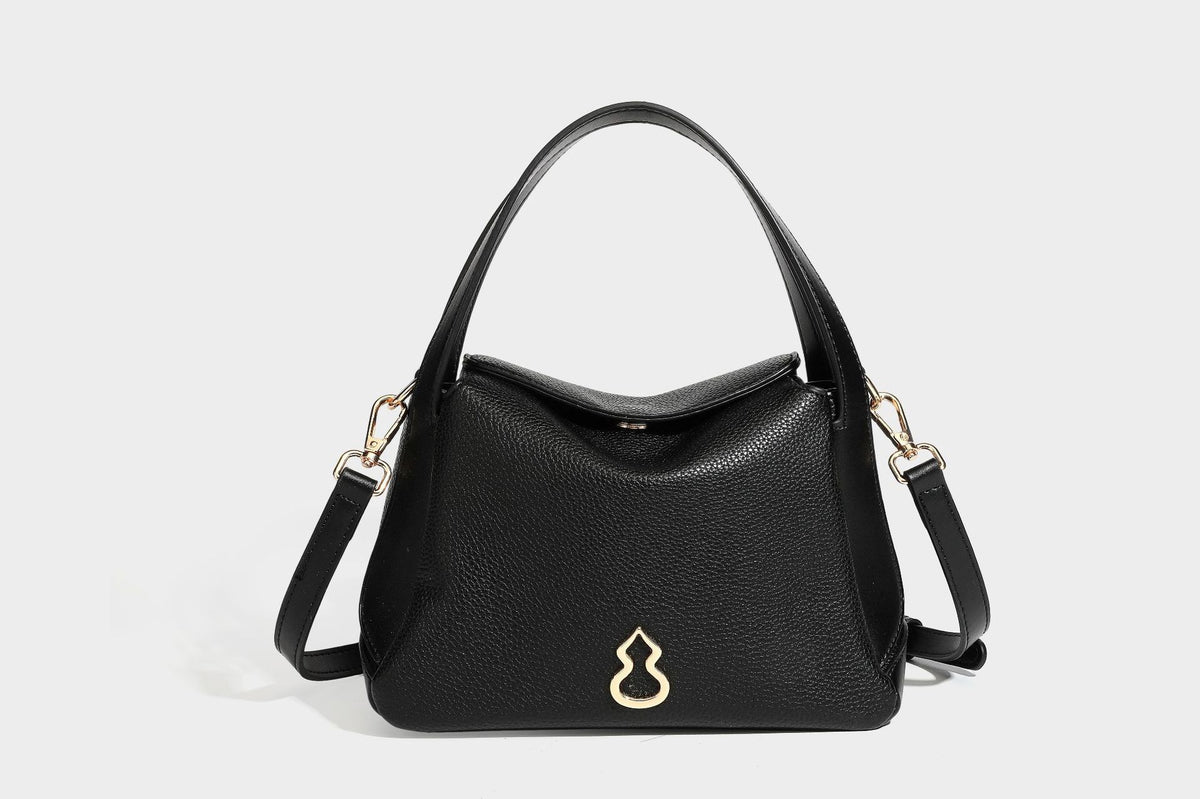 Structured pebbled leather-look shoulder bag with flap top, gold-tone emblem hardware, dual top handles, and detachable