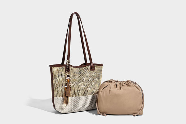 Woven beige and cream tote bag with brown leather-look trim, long double shoulder straps, and knotted tassel charm on front