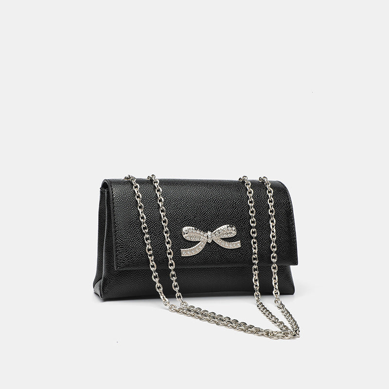 Structured rectangular flap crossbody bag with rhinestone bow and silver chain strap in pebbled finish, detail view 3
