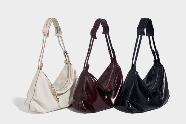 Glossy black slouchy hobo shoulder bag with zip closure, silver-tone ring hardware, and adjustable crossbody strap, detail