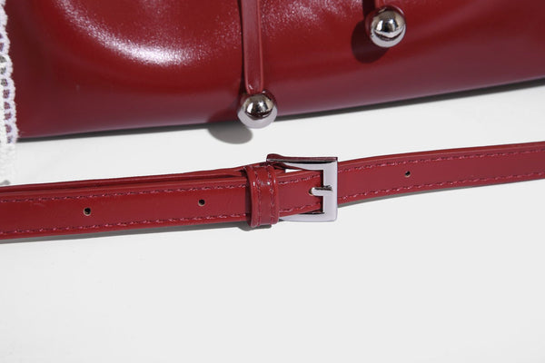 Kleine kuppelförmige Henkeltasche in glänzender Lederoptik mit Kordelzugverschluss, weißem Spitzen-Schleifenanhänger und silberfarbenen Metallbeschlägen
