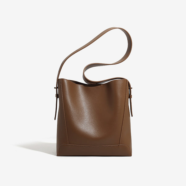 Structured smooth leather-look bucket shoulder bag with long adjustable strap and gold-tone buckle hardware in brown, front