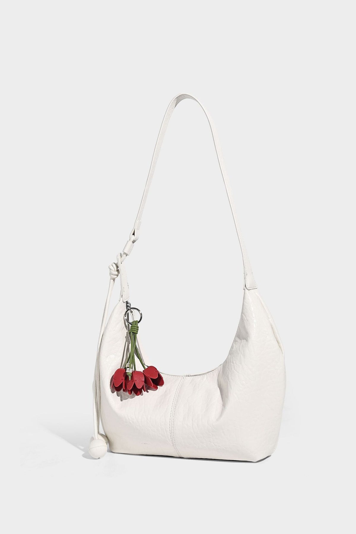 Slouchy crescent half-moon shoulder bag in pink pebbled textured finish with floral charm and knotted side detail, detail