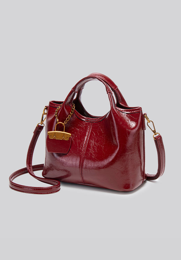 Structured crinkle-gloss top-handle satchel in deep burgundy with antique gold lock charm and detachable shoulder strap