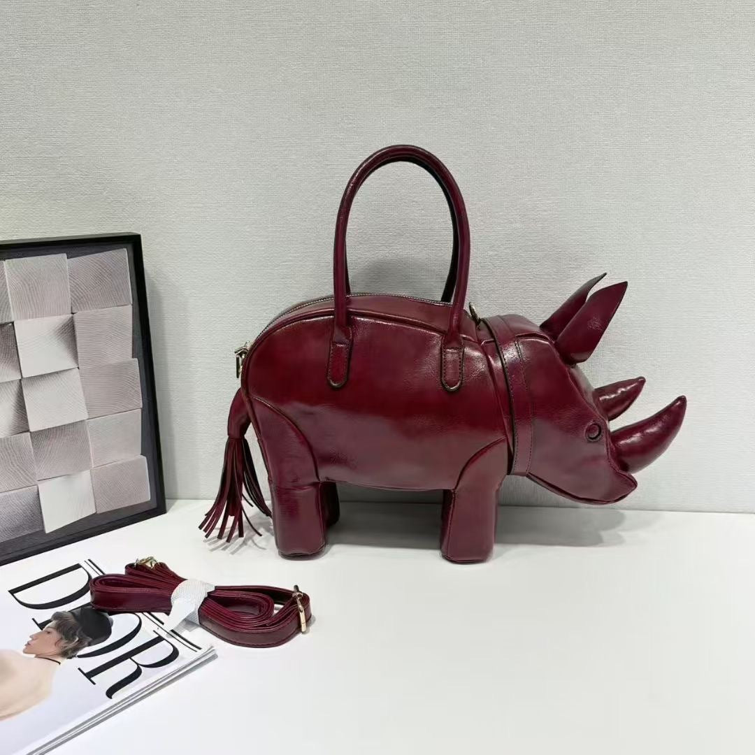 Rhinoceros-shaped 3D structured handbag with sculpted horns, four legs, tassel tail, twin top handles, and detachable, detail