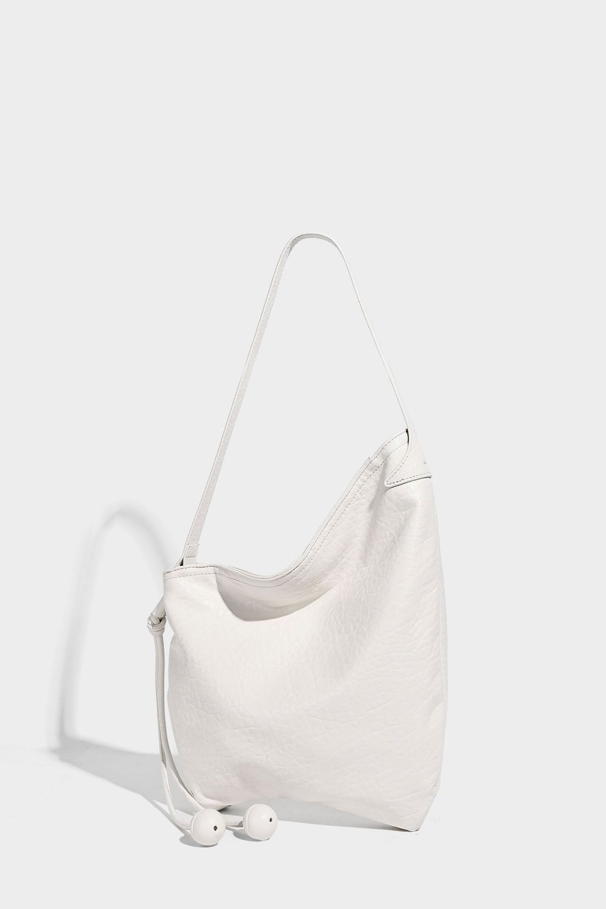 Slouchy hobo shoulder bag in pale yellow with slim strap, drawstring bead closure, and pink tulip floral charm, detail view